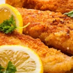 Close-up of crispy fried whiting fillets with a golden-brown crust, garnished with fresh parsley and lemon wedges.