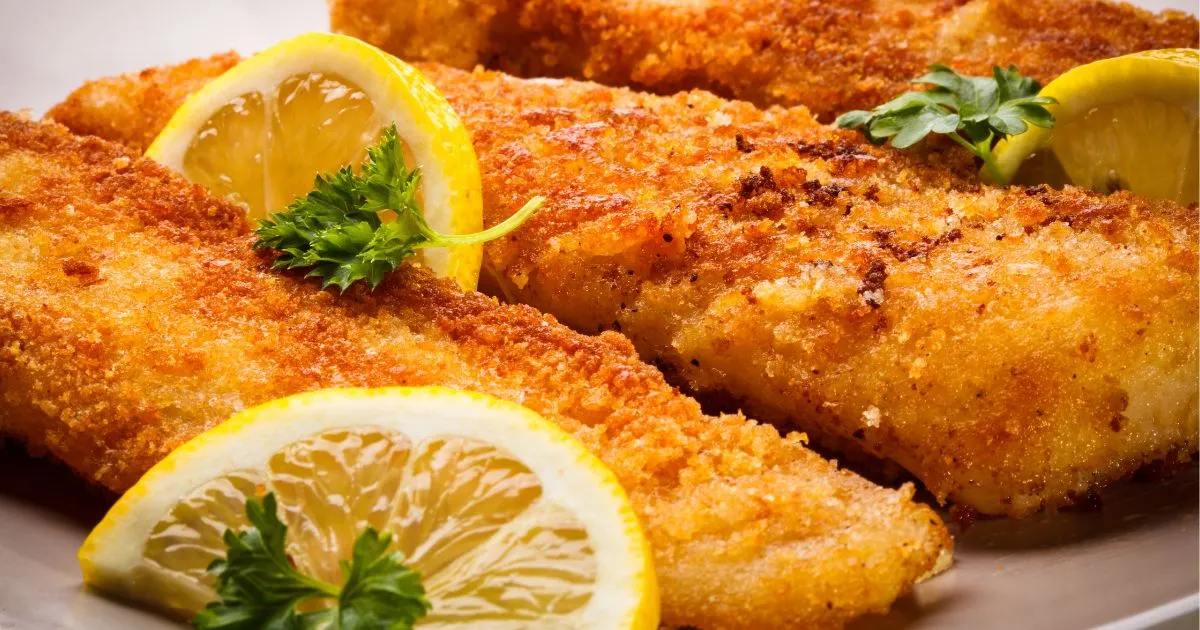 Close-up of crispy fried whiting fillets with a golden-brown crust, garnished with fresh parsley and lemon wedges.